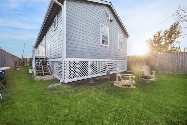 view of side of home featuring a fenced backyard, a fire pit, and a yard