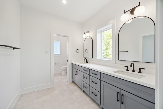 bathroom featuring double vanity, toilet, baseboards, and a sink