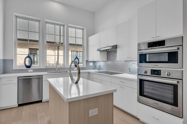 kitchen featuring appliances with stainless steel finishes, a sink, light countertops, under cabinet range hood, and a kitchen island