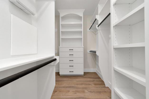 walk in closet featuring a wall mounted AC and light wood-style flooring