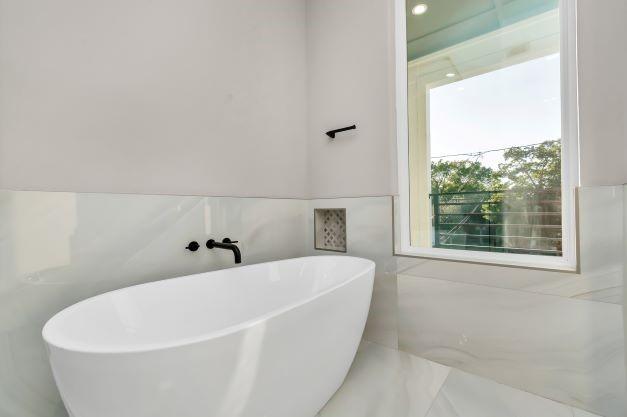 full bathroom with tile walls, a soaking tub, and wainscoting