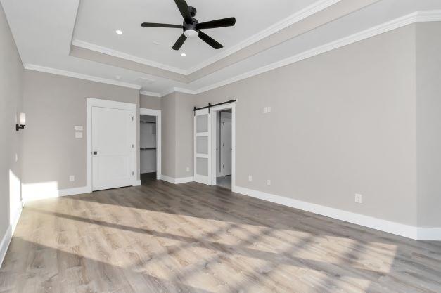 unfurnished bedroom featuring crown molding, baseboards, a raised ceiling, and wood finished floors