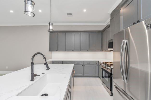 kitchen featuring light stone countertops, appliances with stainless steel finishes, a sink, gray cabinets, and visible vents