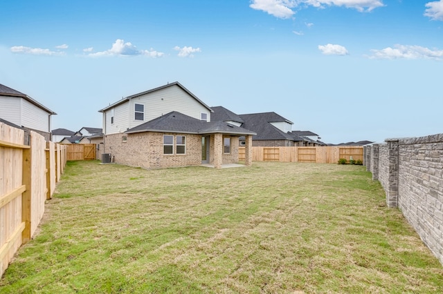 rear view of property featuring a yard, brick siding, central AC unit, and a fenced backyard
