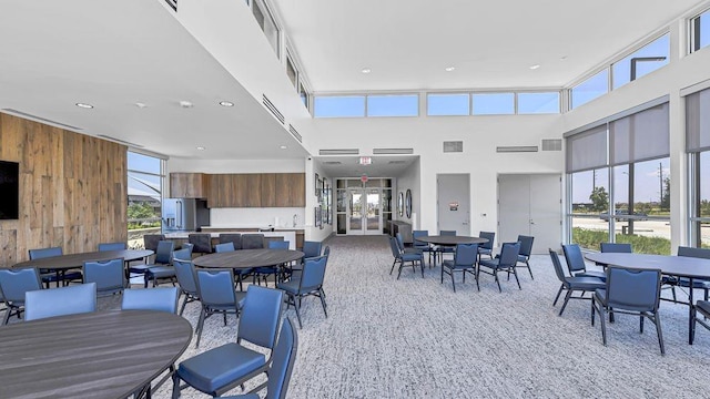 dining space featuring a towering ceiling, wood walls, plenty of natural light, and light carpet