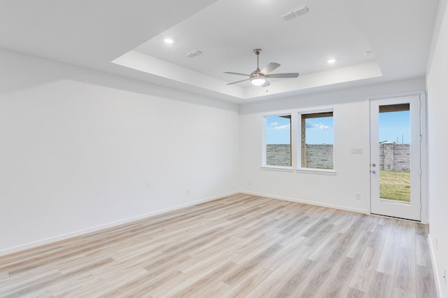 unfurnished room with plenty of natural light, light wood-style flooring, a raised ceiling, and a ceiling fan