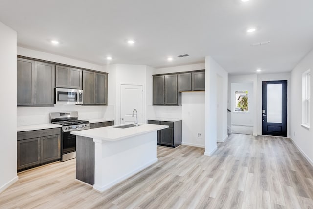 kitchen featuring a kitchen island with sink, appliances with stainless steel finishes, a sink, and light wood-style flooring