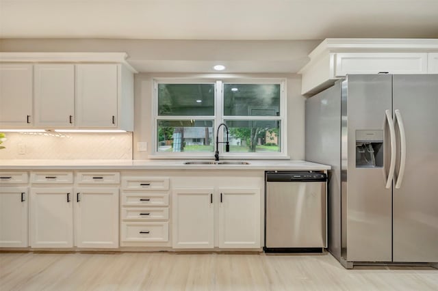 kitchen with appliances with stainless steel finishes, tasteful backsplash, a sink, light countertops, and light wood finished floors