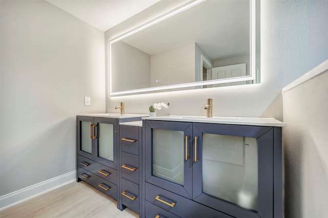 bathroom with double vanity, baseboards, a sink, and wood finished floors