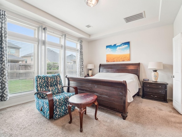 bedroom with a tray ceiling, visible vents, and carpet