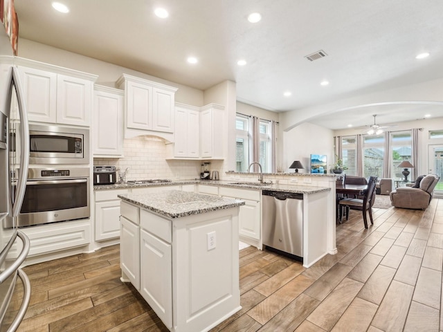 kitchen with visible vents, a peninsula, open floor plan, a ceiling fan, and stainless steel appliances