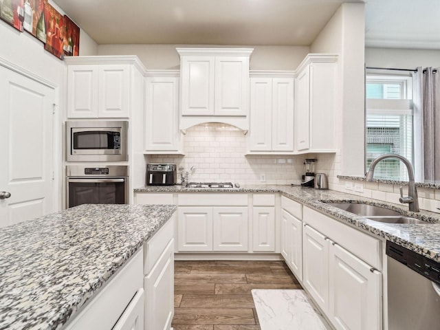 kitchen with wood finished floors, white cabinetry, a sink, appliances with stainless steel finishes, and backsplash