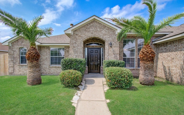 view of exterior entry with brick siding and a lawn