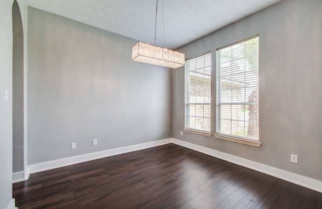 unfurnished dining area with baseboards, a textured ceiling, dark wood finished floors, and a notable chandelier