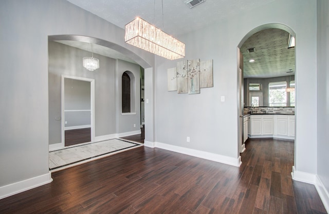 unfurnished dining area with dark wood-style flooring, arched walkways, a sink, baseboards, and a notable chandelier