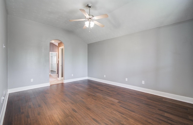 unfurnished room with a ceiling fan, arched walkways, vaulted ceiling, dark wood finished floors, and baseboards