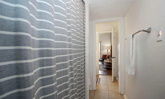 hall featuring light tile patterned flooring, a textured ceiling, and baseboards