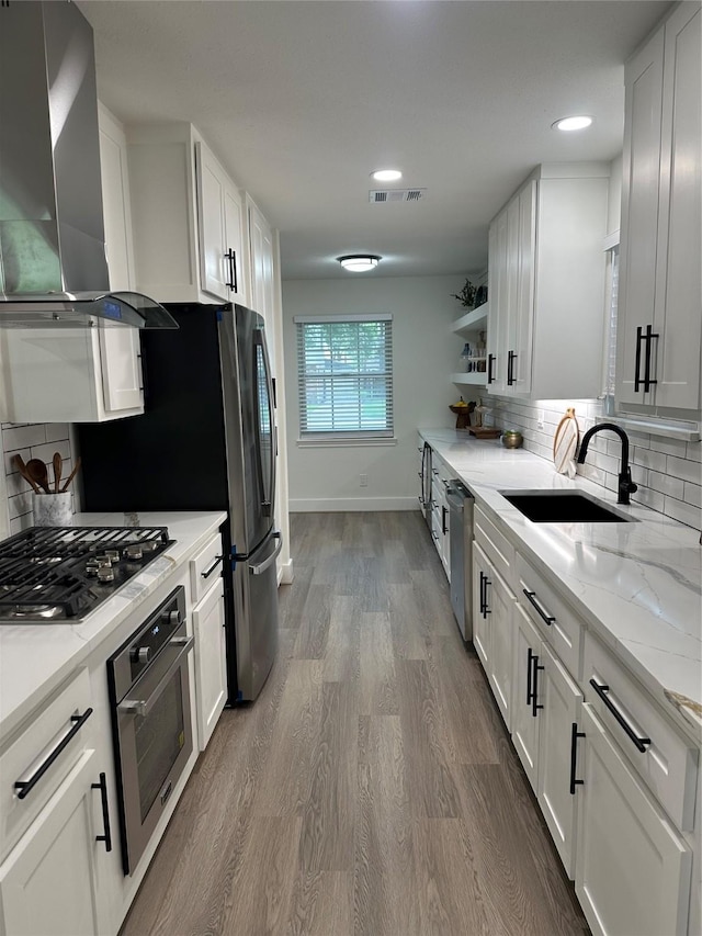 kitchen with wall chimney range hood, appliances with stainless steel finishes, a sink, baseboards, and white cabinetry