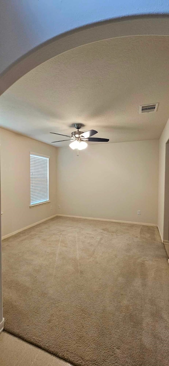 spare room featuring visible vents, light carpet, baseboards, ceiling fan, and a textured ceiling