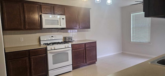 kitchen with dark brown cabinetry, white appliances, baseboards, light floors, and backsplash