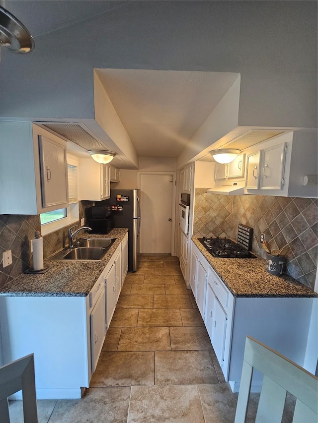 kitchen with stone tile floors, decorative backsplash, white cabinetry, a sink, and black gas stovetop