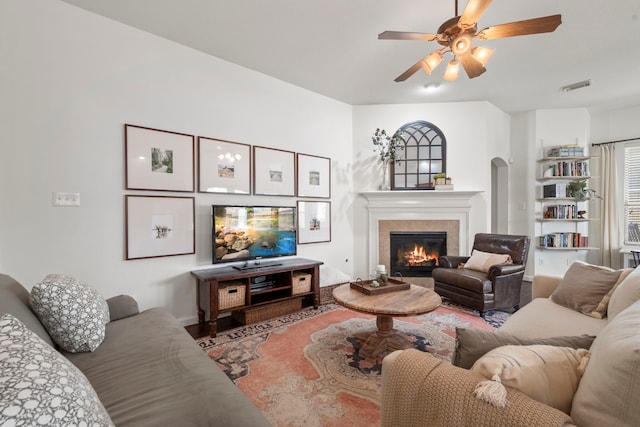 living area featuring arched walkways, a ceiling fan, wood finished floors, a tile fireplace, and visible vents