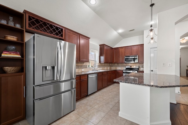 kitchen featuring a sink, dark stone counters, stainless steel appliances, lofted ceiling, and tasteful backsplash