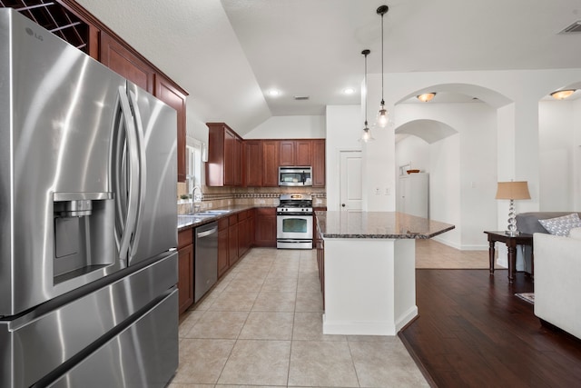 kitchen featuring decorative backsplash, appliances with stainless steel finishes, a sink, dark stone countertops, and lofted ceiling