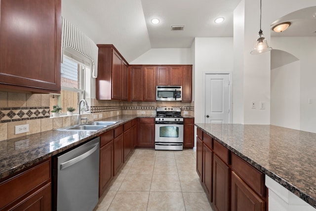 kitchen with dark stone counters, a sink, appliances with stainless steel finishes, backsplash, and vaulted ceiling