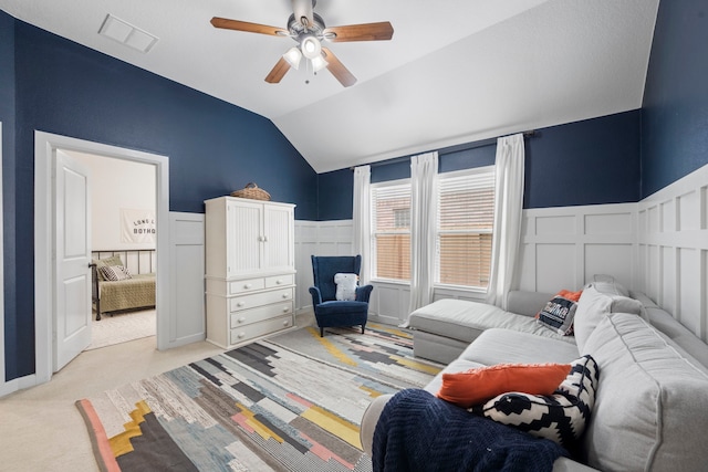 bedroom featuring light colored carpet, visible vents, wainscoting, lofted ceiling, and a decorative wall