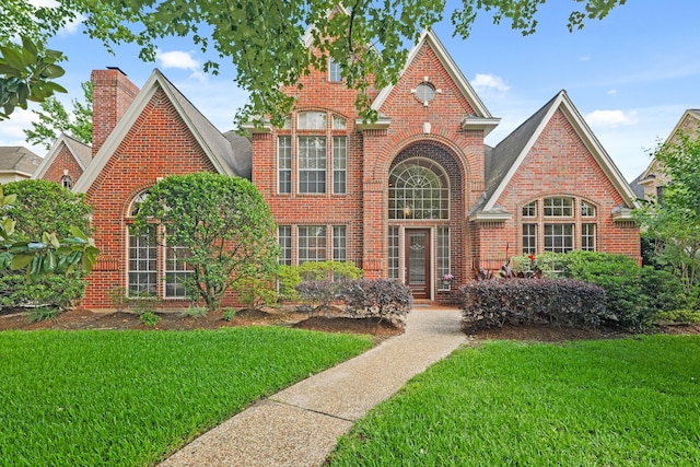 view of front facade featuring a chimney, a front lawn, and brick siding