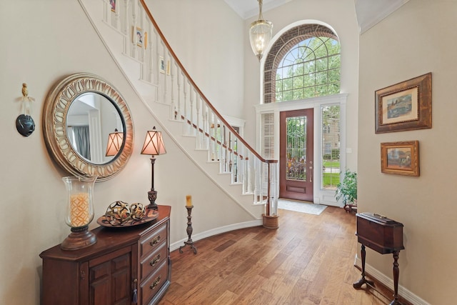 entryway with ornamental molding, stairs, a towering ceiling, baseboards, and light wood-type flooring