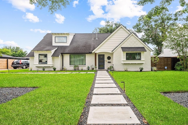view of front of home with fence, a shingled roof, a front lawn, and brick siding