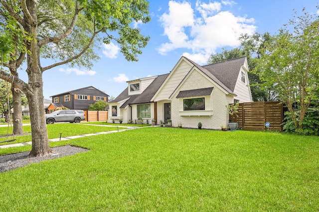 modern farmhouse featuring fence, a front yard, roof with shingles, and brick siding