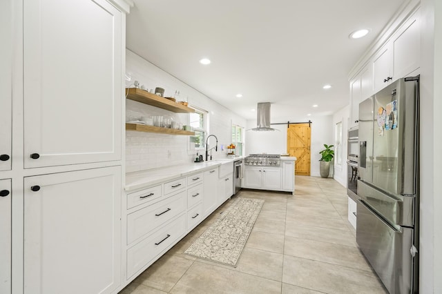 kitchen featuring appliances with stainless steel finishes, a barn door, recessed lighting, island exhaust hood, and tasteful backsplash