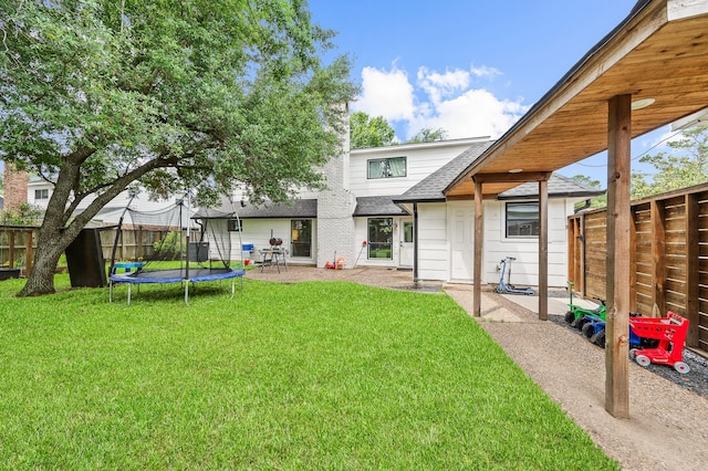 rear view of house featuring roof with shingles, a trampoline, a fenced backyard, a patio area, and a lawn
