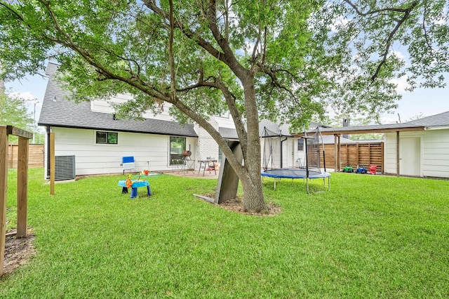 back of property with a patio, a fenced backyard, roof with shingles, a trampoline, and a yard