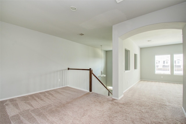 carpeted empty room featuring baseboards, arched walkways, and visible vents
