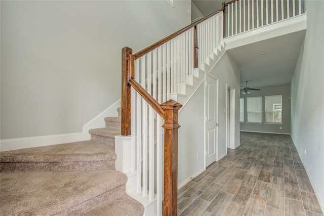 stairway featuring baseboards, a high ceiling, ceiling fan, and wood finished floors