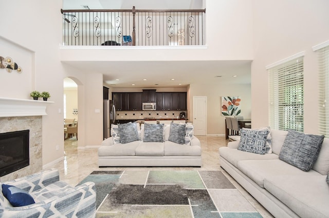 living area with arched walkways, baseboards, marble finish floor, a high ceiling, and a premium fireplace