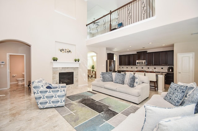 living area featuring a high end fireplace, arched walkways, baseboards, and a towering ceiling