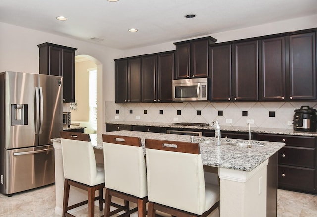 kitchen with decorative backsplash, arched walkways, light stone counters, a sink, and appliances with stainless steel finishes