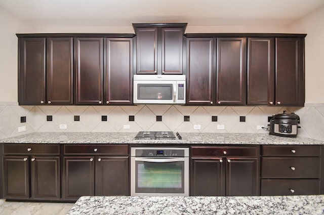 kitchen with appliances with stainless steel finishes, dark brown cabinets, light stone countertops, and tasteful backsplash