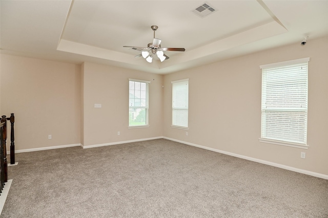 carpeted spare room featuring visible vents, baseboards, ceiling fan, and a tray ceiling