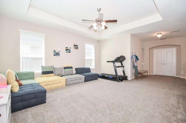 carpeted living area featuring a raised ceiling, baseboards, a ceiling fan, and visible vents