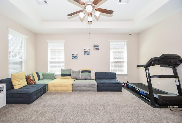 workout room with carpet flooring, ceiling fan, visible vents, and a raised ceiling