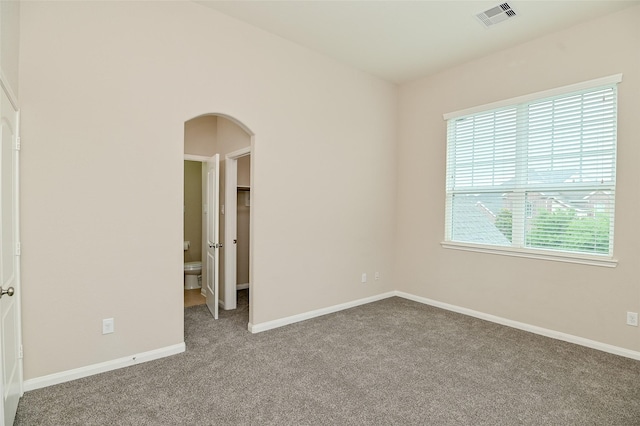 unfurnished bedroom with visible vents, arched walkways, baseboards, and carpet flooring