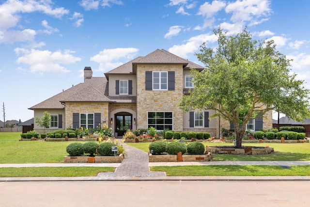 view of front of house featuring a front yard, stone siding, roof with shingles, french doors, and a chimney