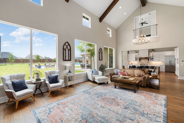 living area with wood finished floors, high vaulted ceiling, beamed ceiling, a notable chandelier, and a wealth of natural light