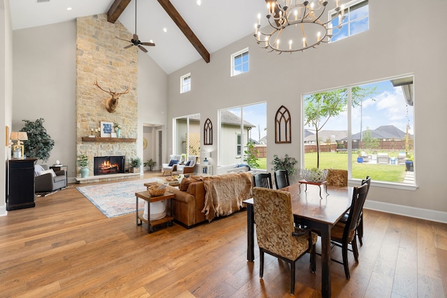 dining space featuring a fireplace, light wood-type flooring, beam ceiling, high vaulted ceiling, and ceiling fan with notable chandelier